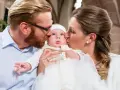 Eltern küssen ihr Baby bei der Taufe. Die Frage, wie viele Paten darf man haben, beschäftigt viele.