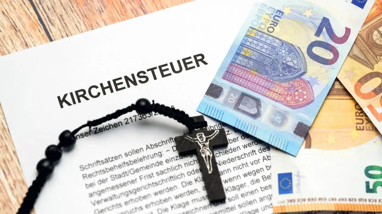 Ein Dokument mit der Aufschrift "Kirchensteuer" liegt neben Euro-Scheinen und einem Rosenkranz. Der Kirchensteuer prozentuale Anteil ist hier symbolisch dargestellt.