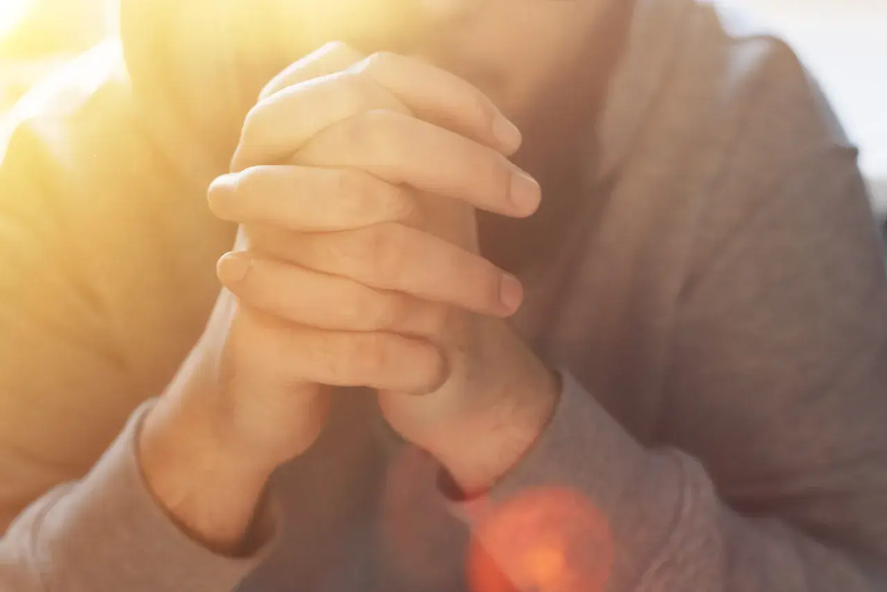 Hände im Gebet, die an das "Vater unser im Himmel" erinnern. Warmes Licht fällt auf die gefalteten Finger.