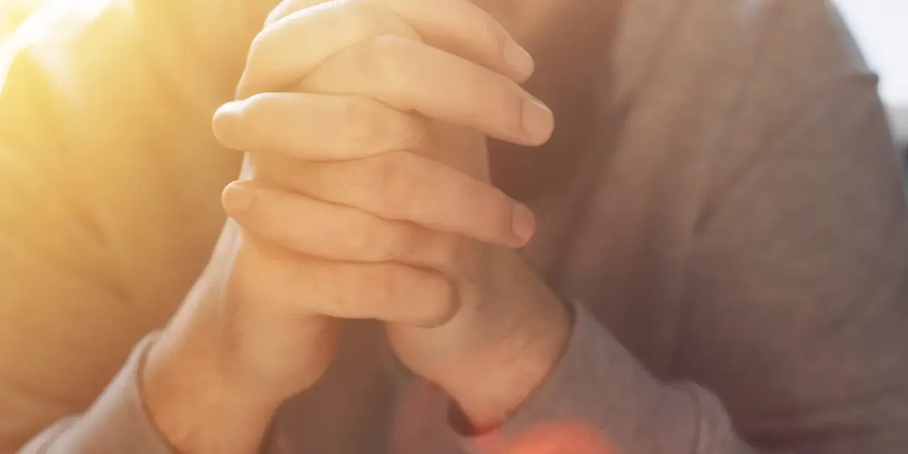 Hände im Gebet, die an das "Vater unser im Himmel" erinnern. Warmes Licht fällt auf die gefalteten Finger.