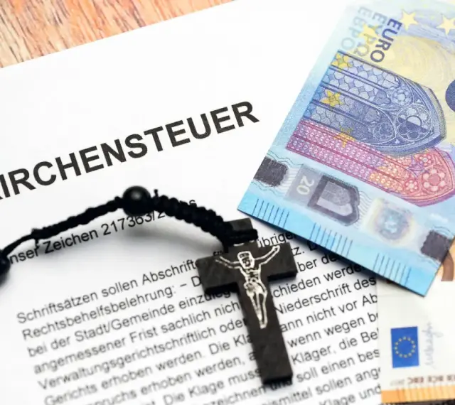 Ein Dokument mit der Aufschrift "Kirchensteuer" liegt neben Euro-Scheinen und einem Rosenkranz. Der Kirchensteuer prozentuale Anteil ist hier symbolisch dargestellt.