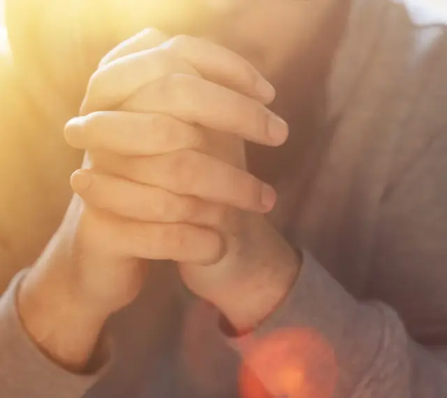 Hände im Gebet, die an das "Vater unser im Himmel" erinnern. Warmes Licht fällt auf die gefalteten Finger.