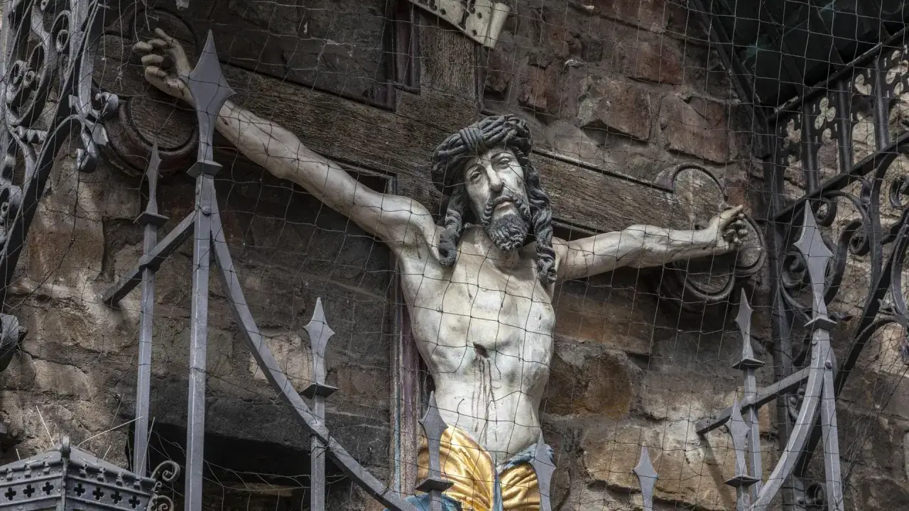 Skulptur von Jesus Christus am Kreuz, mit Dornenkrone und Wunden. Ein Gitter schützt die Darstellung.