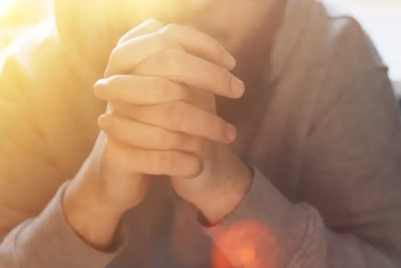 Hände im Gebet, die an das "Vater unser im Himmel" erinnern. Warmes Licht fällt auf die gefalteten Finger.